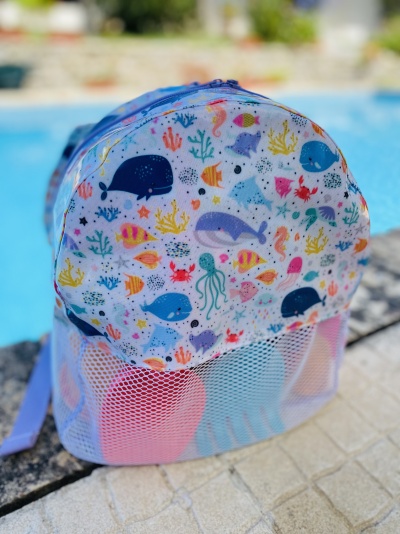 Mochila infantil com padrão marinho colorido e bolso frontal em malha junto à piscina