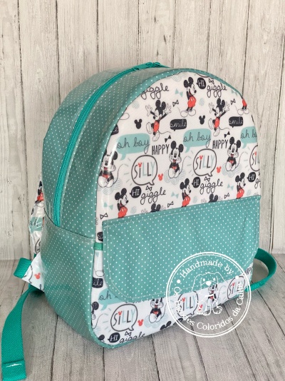 Mochila infantil verde água com padrão de bolinhas brancas e desenhos do Mickey Mouse com várias palavras em inglês.