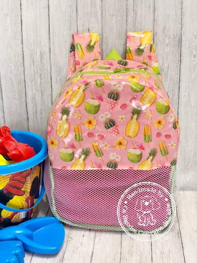 Mochila rosa com padrão tropical e bolso de rede, sobre chão de madeira clara com brinquedos azuis e balde colorido
