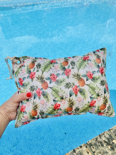 Almofada tropical colorida segurada por uma mão junto a uma piscina