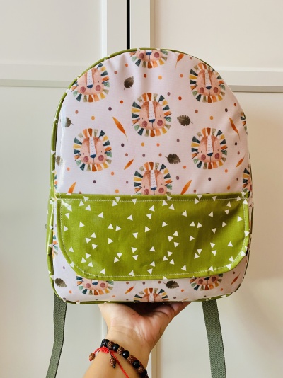 Mochila infantil rosa claro com estampado de leões e bolso verde com triângulos brancos