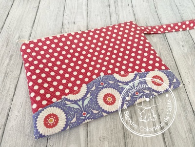 Bolsa de mão vermelha com bolinhas brancas e azul com flores sobre chão de madeira clara