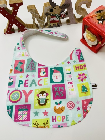 Babete de tecido com padrão natalício colorido e decoração de Natal em fundo branco