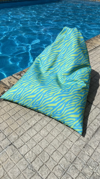 Pufe colorido azul e verde com padrão de zebra junto a piscina