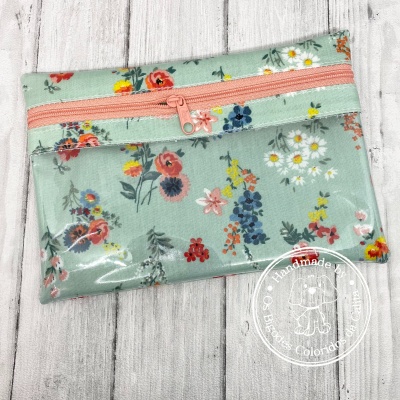 Estojo floral verde-água claro com fecho zip cor-de-rosa sobre superfície de madeira