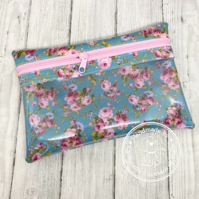 Estojo retangular com padrão floral sobre fundo azul e fecho rosa