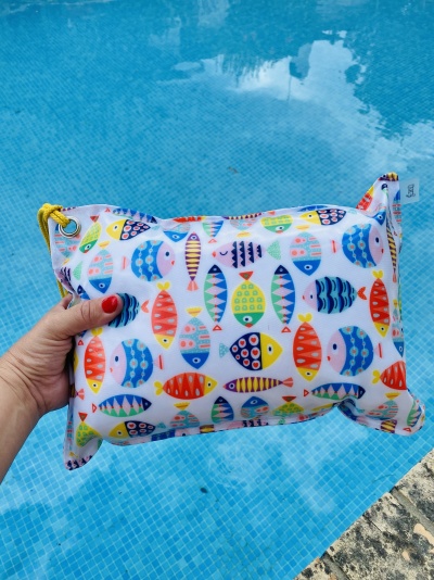Almofada colorida com padrão de peixes segurada junto a piscina