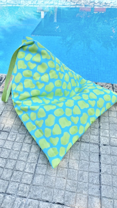 Pufe triangular macio com padrão amarelo e azul junto a piscina