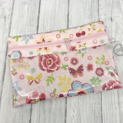 Estojo rosa com padrão floral e borboletas sobre fundo de madeira branca.