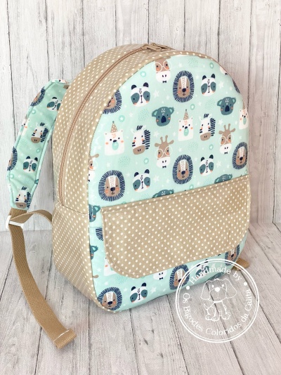Mochila infantil em tecido com padrão de animais e bolinhas, alças ajustáveis, fundo madeira clara