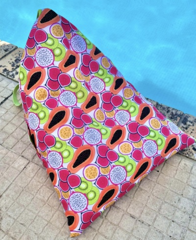 Almofada triangular colorida com padrão de frutas junto à piscina