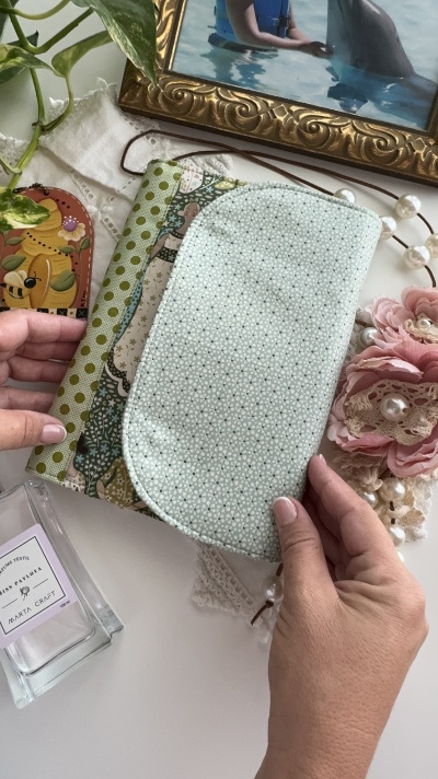 Estojo de tecido verde e branco com padrão floral, mãos segurando estojo aberto