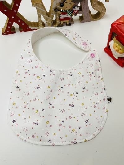 Babete branco com estrelas coloridas, fecho de pressão rosa, decoração de Natal ao fundo