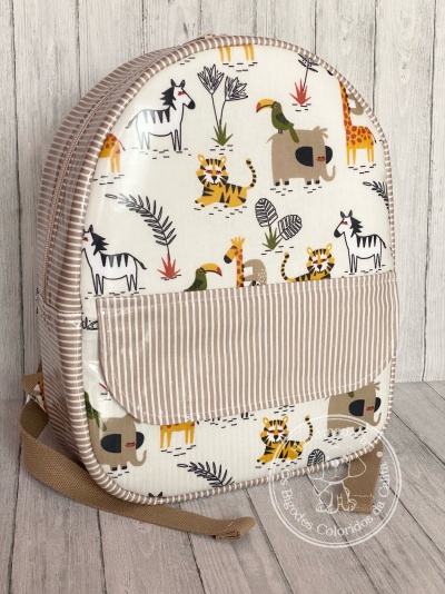 Mochila infantil estampada com animais e bolso riscado sobre fundo madeira clara