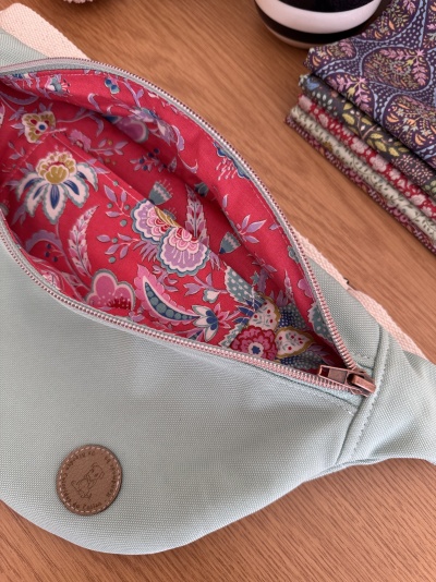 Bolsa tipo cinto verde-água com fecho rosa e forro vermelho floral