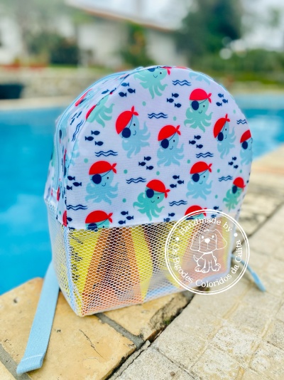 Mochila infantil com padrão de polvos azuis com chapéus vermelhos junto a piscina