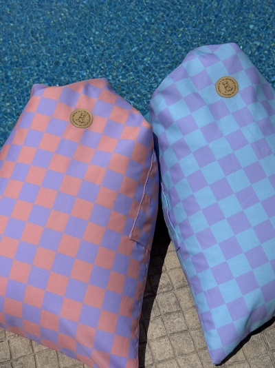 Duas almofadas com padrão quadriculado rosa e lilás e azul clara e lilás junto a piscina