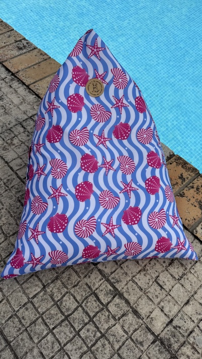 Almofada triangular azul com padrão de conchas e estrelas do mar cor-de-rosa junto à piscina