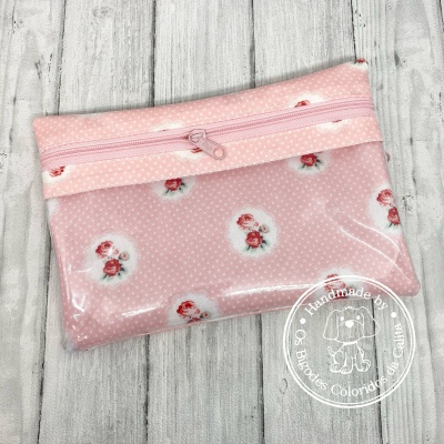 Bolsa plástica rosada com flores vermelhas e fecho de correr rosa, sobre madeira clara.