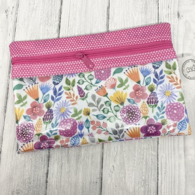 Bolsa de tecido com padrão floral colorido e zíper rosa com pontos brancos sobre madeira