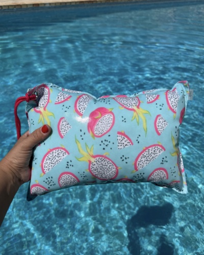 Mala azul clara com padrão de frutas do dragão segurada junto a uma piscina