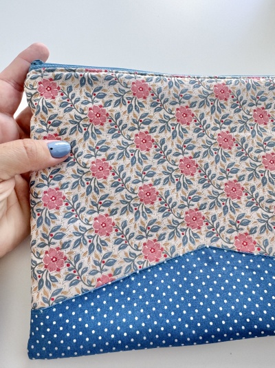 Estojo de tecido com padrão floral vermelho e bolinhas brancas sobre fundo azul.