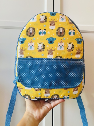 Mochila infantil em tecido amarelo com animais e bolso azul com pontos brancos.