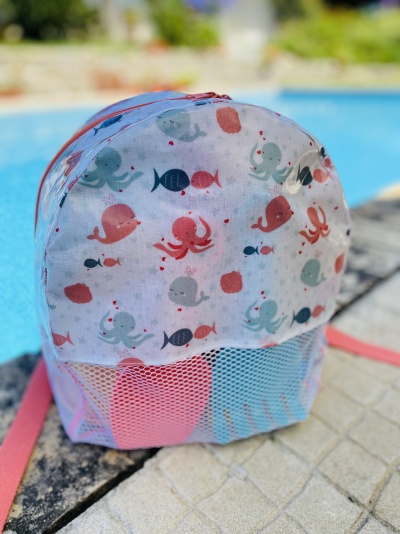 Mochila pequena com padrão de animais marinhos coloridos e bolso em rede branca perto da piscina