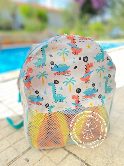 Mochila infantil com padrão de dinossauros e bolso dianteiro em rede junto a piscina
