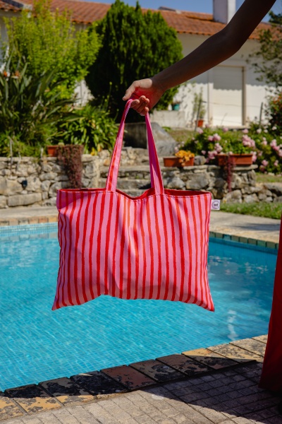 Mala de tecido rosa com riscas vermelhas junto a piscina ao sol
