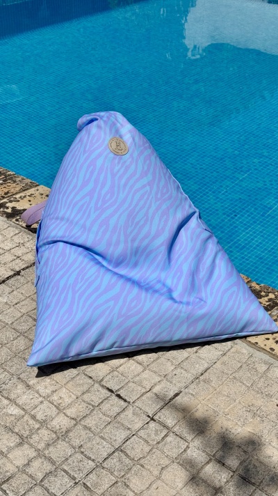 Puff triangular lilás com padrão zebrado junto a piscina