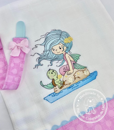 Fralda bordada com menina sereia e tartaruga, fita rosa e prendedor azul