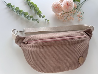 Bolsa de cintura castanha clara com alça bege e flores ao fundo