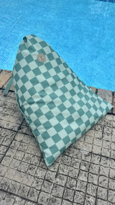 Almofada saco de feijão quadriculada verde e branca ao lado de piscina