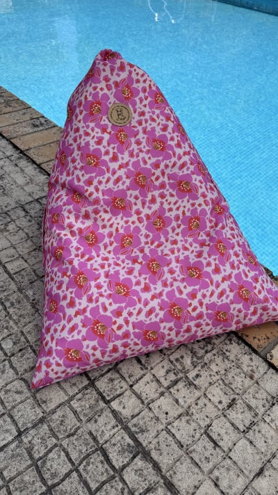 Pufe triangular de tecido rosa com flores vermelhas ao lado de piscina