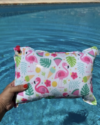 Mala impermeável com padrão colorido de flamingos e frutas segura em frente a uma piscina