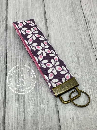 Porta-chaves em tecido floral rosa e branco com argola metálica sobre fundo de madeira cinza