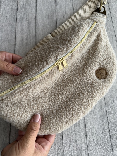 Mala pochete creme felpudo com fecho amarelo e etiqueta de couro sobre fundo de madeira clara