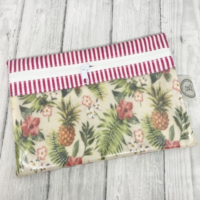 Bolsa com padrão floral de abacaxi e flores, fecho branco, faixa riscada cor-de-rosa e branca, sobre madeira clara