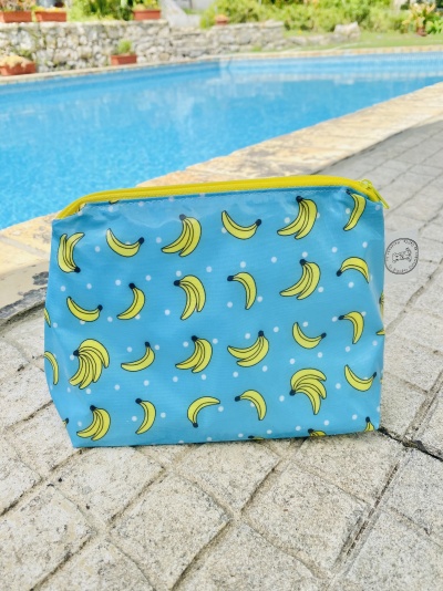 Necessaire azul com padrão de bananas amarelas e pontos brancos junto a piscina