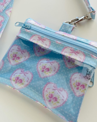 Carteira azul com padrão de corações brancos, flores rosas e laços, com fecho e alça.
