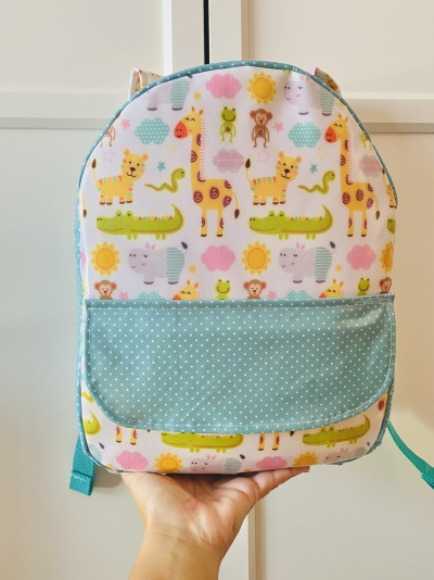 Mochila infantil com padrão de animais coloridos e bolso azul com bolinhas