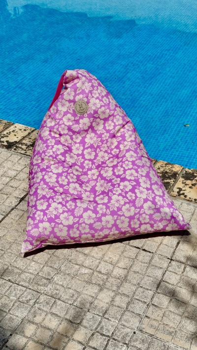 Puff triangular rosa com padrão floral branco ao lado de piscina