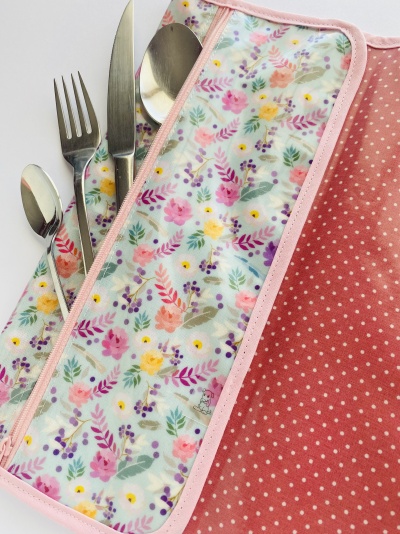 Conjunto de talheres em bolsa com padrão floral e tecido rosa de bolinhas.