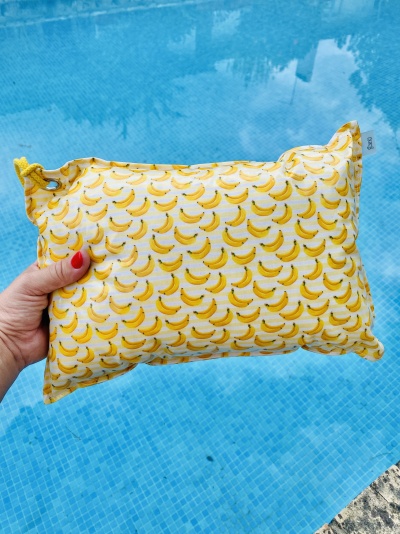 Almofada pequena com padrão de bananas amarelas à frente de piscina azul