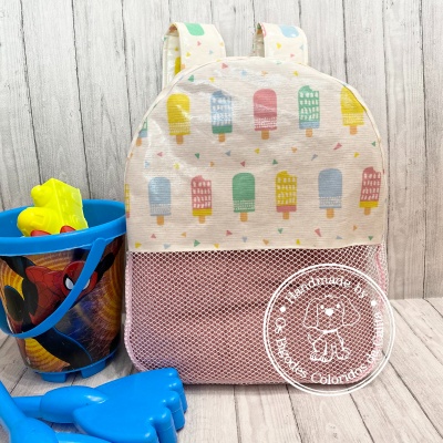 Mochila infantil bege com padrão de gelados coloridos e balde azul com desenho do Homem-Aranha e brinquedos.