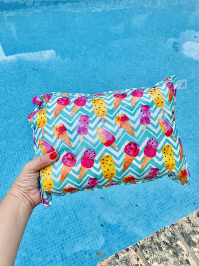 Mala pequena com padrão de gelados coloridos segurada junto a piscina de água azul