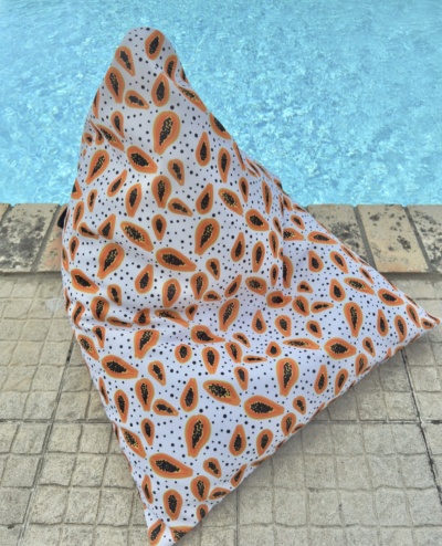 Pufe triangular com padrão de folhas laranja e preto junto a piscina