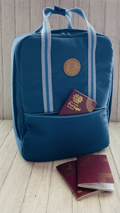 Mochila azul com passaportes portugueses num bolso frontal e em frente numa superfície de madeira
