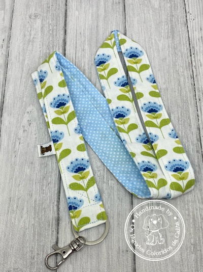 Correia floral azul e verde com gancho metálico sobre madeira clara